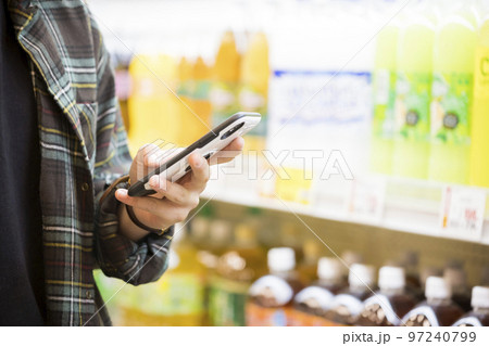 スマホを持ってスーパーで買い物をする若い男性手元 97240799
