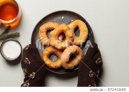 mittened hands hold a plate of donuts. Top view on a light background, with a drink in a cup and fir branches 97241689