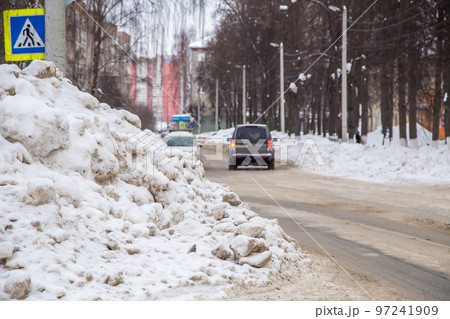 A large, high snowdrift against the backdrop of a city street with cars. A large, high snowdrift against the backdrop of a city street with cars. 97241909