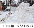 A huge, dirty snowdrift against the backdrop of a city street with cars.  97241913