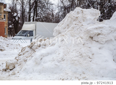 A huge, dirty snowdrift against the backdrop of a city street with cars. A huge, dirty snowdrift against the backdrop of a city street with cars. 97241913