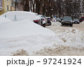 A large snowdrift against the backdrop of a city street with cars. 97241924