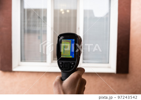 A male hand holds a thermal imager at the window of a house. Search for heat loss in private houses 97243542