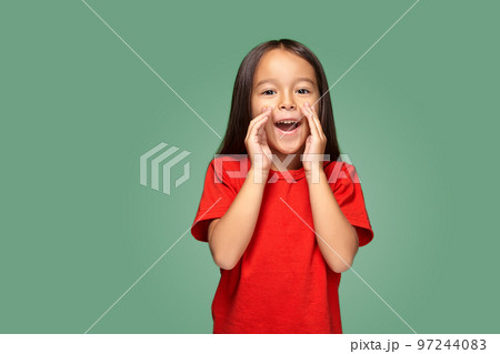 Portrait of a small pretty girl standing sideways and calling someone holding her hand near her mouth 97244083