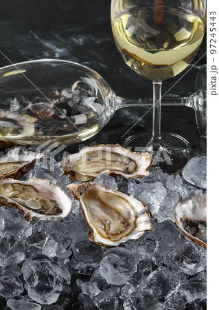Fresh opened oysters in ice and champagne on a black stone textured background. Side view. Close-up shot. 97245443