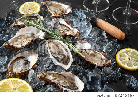 Fresh opened oysters, ice and lemon on a black stone textured background. Top view. Close-up shot. 97245467