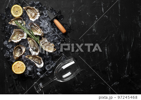 Fresh opened oysters, ice and lemon on a black stone textured background. Top view with copy space. Close-up shot. 97245468