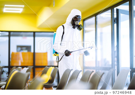 Man wearing protective suit disinfecting assembly hall with spray. Disinfecting of office. COVID-19. 97246948