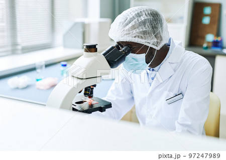 Black male scientist looking in microscope working in laboratory Black male scientist looking in microscope working in laboratory 97247989