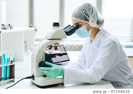 Young female scientist looking in microscope 97248010