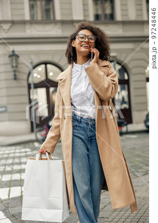 Smiling afro american woman after shopping with paper bags and phone while walking in city 97248446