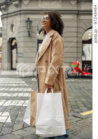 Fashion afro american woman after successful shopping with paper bags crosses the road in city Fashion afro american woman after successful shopping with paper bags crosses the road in city 97248464