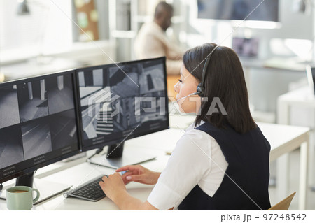 Young woman looking at surveillance camera feeds in security office 97248542
