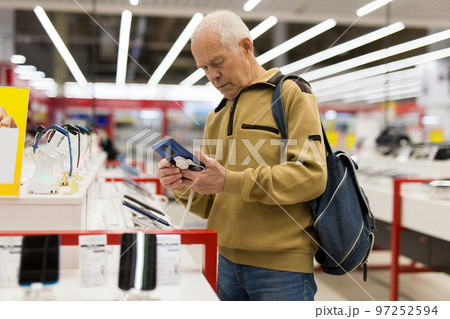 elderly man examines tablet computer in showroom of electronics store 97252594