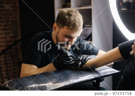 Handsome tattoo master making black tattoo with paint. Master works in black sterile gloves. Young tattoo artist in work 97255758