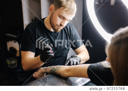 Tattoo master is tattooing a woman's hand. Wireless tattoo machine, safety and hygiene at work. Close-up of tattoo artist work. Tattoo salon 97255768