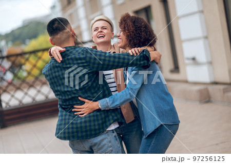 Company of three friends embracing one another outdoors 97256125