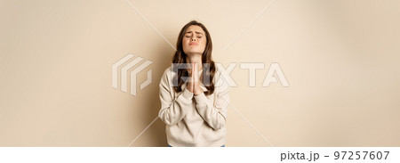 Woman begging and pleading god, supplicating, say please, standing desperate over beige background 97257607