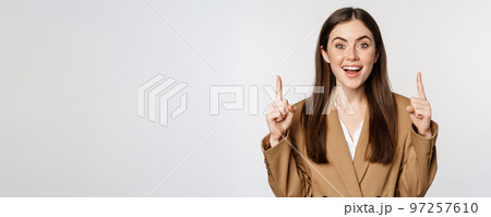 Portrait of female entrepreneur, corporate woman pointing fingers up, smiling confident, showing advertisement, logo on top, white background 97257610