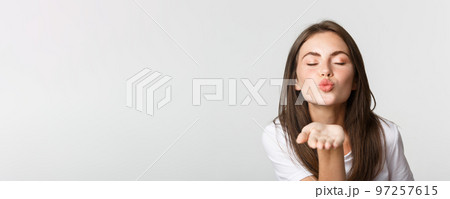 Close-up of beautiful flirty girl pouting lips and sending air kiss at camera 97257615