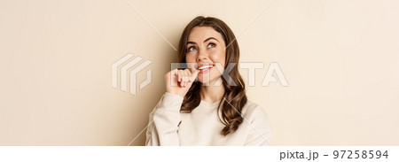 Cute modern woman thinking, daydreaming and smiling, looking up thoughtful, standing over beige background 97258594