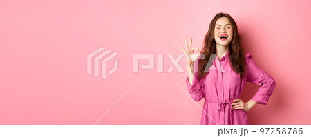 Young attractive woman saying yes, showing okay sign in approval, smiling confident and satisfied, standing over pink background 97258786