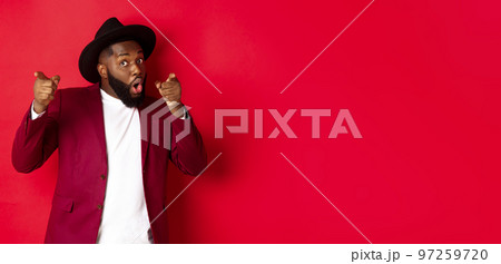 Christmas and people concept. Happy Black man celebrating New Year and dancing, wearing party outfit, red background 97259720