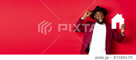 Real estate. Cheerful Black man showing paper house and smiling, recommending broker, standing over red background 97260170