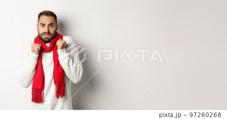 Christmas holidays and celebration concept. Scared man trembling from fear and looking startled, standing anxious in red scarf and white sweater 97260268