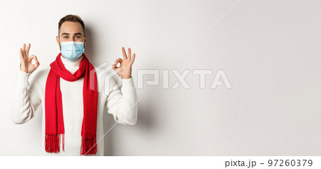 Covid-19, lockdown and quarantine concept. Satisfied handsome guy in face mask showing okay sign, approve or agree, like something, white background 97260379