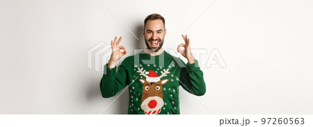 Christmas, holidays and celebration. Satisfied handsome guy in sweater, showing okay signs and smiling, praise something great, standing over white background 97260563