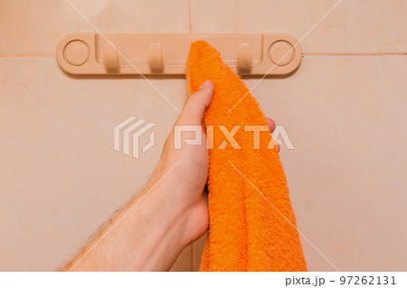 Man's hand takes an orange towel in the bathroom. Care and hygiene concept 97262131