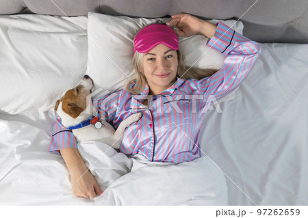 An attractive young woman wearing pajamas is holding a dog while laying on a bed 97262659
