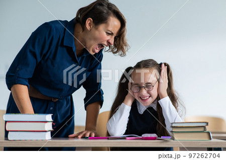 A female teacher yells at a student. Little girl covers her ears with her hands. A female teacher yells at a student. Little girl covers her ears with her hands. 97262704