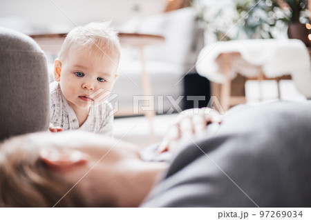 Happy family moments. Mother lying comfortably on children's mat playing with her baby boy watching and suppervising his first steps. Positive human emotions, feelings, joy 97269034