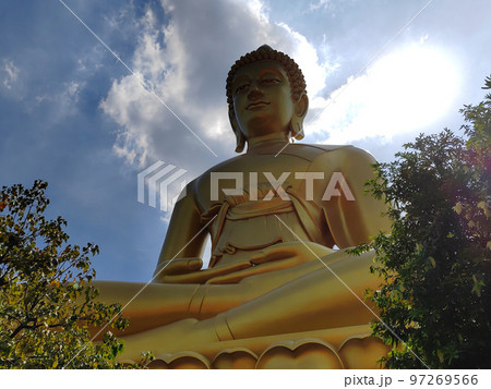 Golden big Buddha statue in Wat Pak Nam Phasi Charoen temple. Sunlight sky and cloud background 97269566