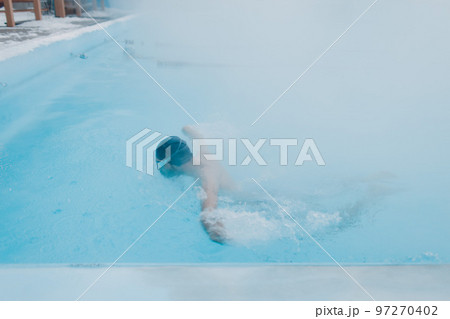 Fit swimmer male training swim in open winter swimming pool with fog. Geothermal outdoor spa health concept. Fit swimmer male training swim in open winter swimming pool with fog. Geothermal outdoor spa health concept. 97270402