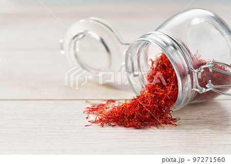 Dried saffron spices spill out of a glass storage jar, on a wooden table. 97271560