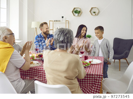 Big family congratulates child boy and clapping hands during family dinner in living room. 97273545