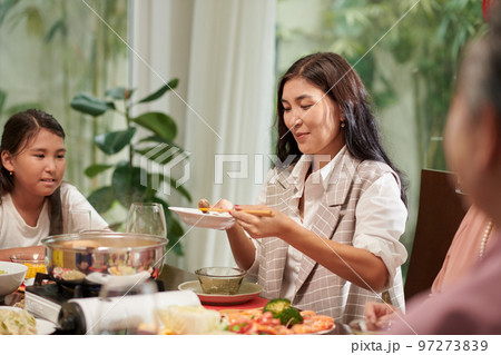 Smiling mature woman filling her plate at family dinner Smiling mature woman filling her plate at family dinner 97273839