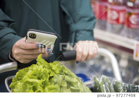 スーパーでスマホを持って買い物をする若い女性手元 97277408