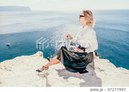 Digital nomad, Business woman working on laptop by the sea. Pretty lady typing on computer by the sea at sunset, makes a business transaction online from a distance. Freelance, remote work on vacation 97277997
