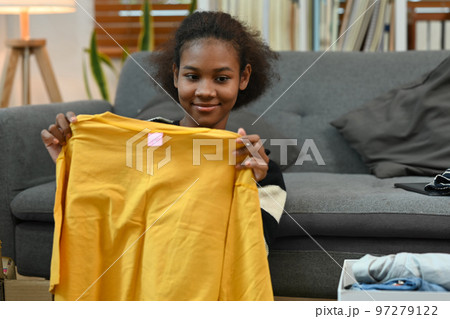 Positive young woman packing clothes into donation box while sitting in living room. Charity, donation and reuse recycle concept Positive young woman packing clothes into donation box while sitting in living room. Charity, donation and reuse recycle concept 97279122