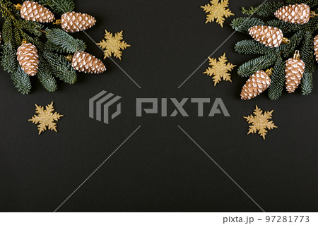 Green branches of a Christmas tree with decorations in the form of golden cones and snowflakes on a black background with a place for text. Top view 97281773