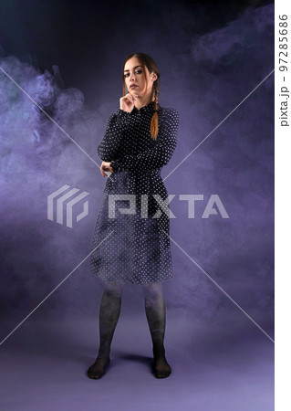a girl in a black dress and pigtails looks at the camera.purple background with smoke 97285686