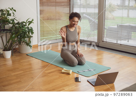 Afro american woman talking with fitness instructor by video call before online classes at home  97289063