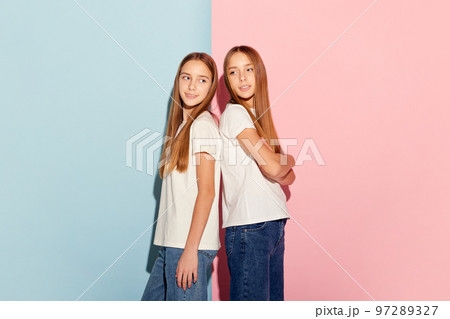 Friends. Two beautiful teen girls, siblings in t-shirts and jeans posing isolated over duotone pink-blue background. Emotions, family, fun, joy, leisure activities concept Friends. Two beautiful teen girls, siblings in t-shirts and jeans posing isolated over duotone pink-blue background. Emotions, family, fun, joy, leisure activities concept 97289327