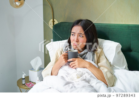 Flu, sickness and people. Young woman feeling sick, having fever and catching col, lying in bed with hot tea, taking drugs from influenza Flu, sickness and people. Young woman feeling sick, having fever and catching col, lying in bed with hot tea, taking drugs from influenza 97289343