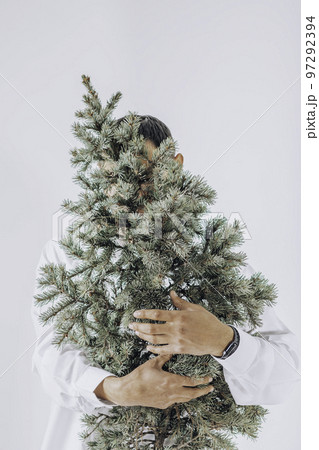 Young man hold in hands Christmas tree, fir branches. Minimal fashion festive Christmas and New Year celebration concept. hugging 97292394