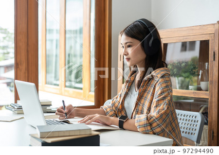 Young woman student in headphone is learning lessons online on laptop with lecturer and taking notes 97294490
